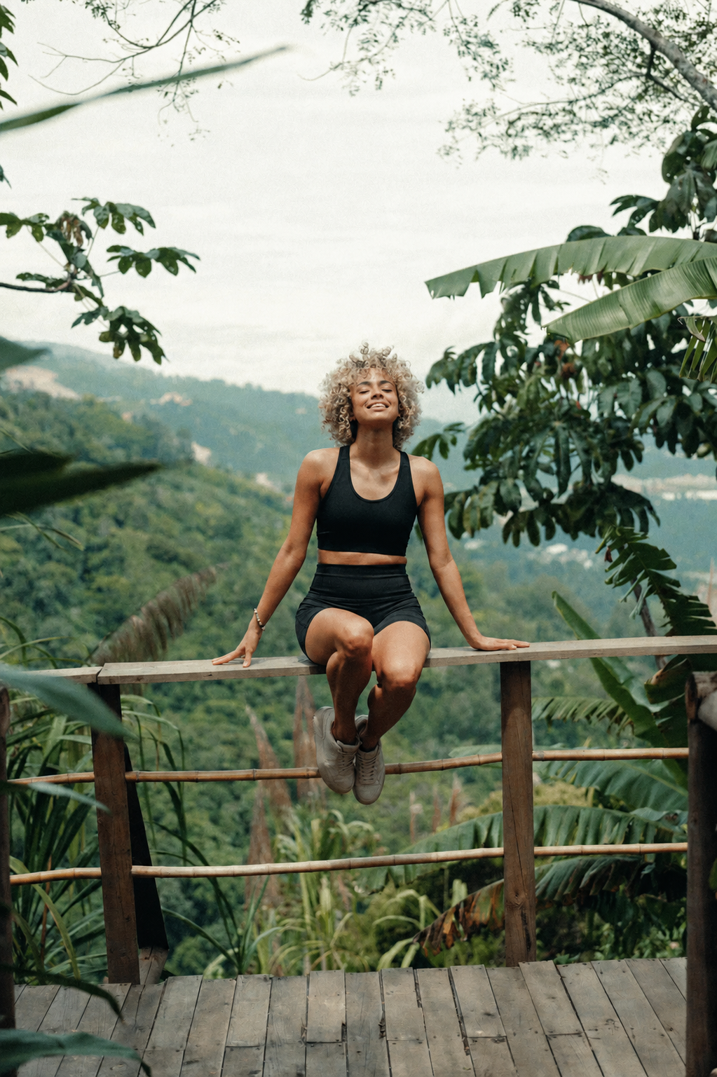 Woman seated on a railing overlooking lush hills